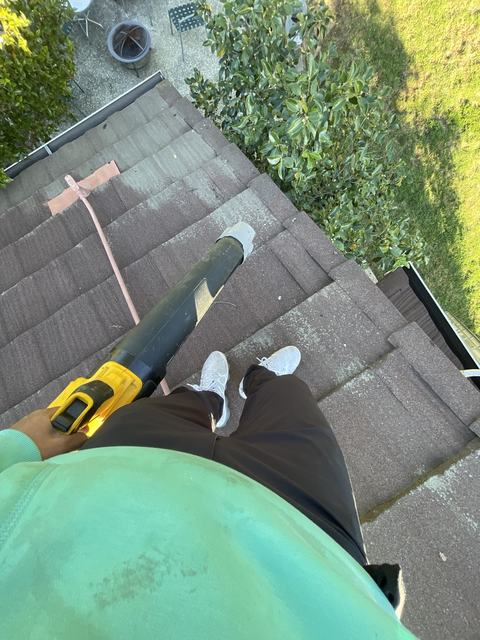 Looking down from a roof, holding a leaf blower over the gutter